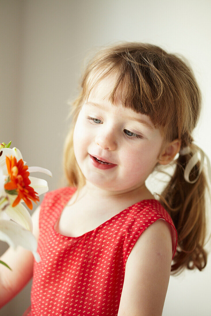 Three year old girl stands in red dress with cut flowers