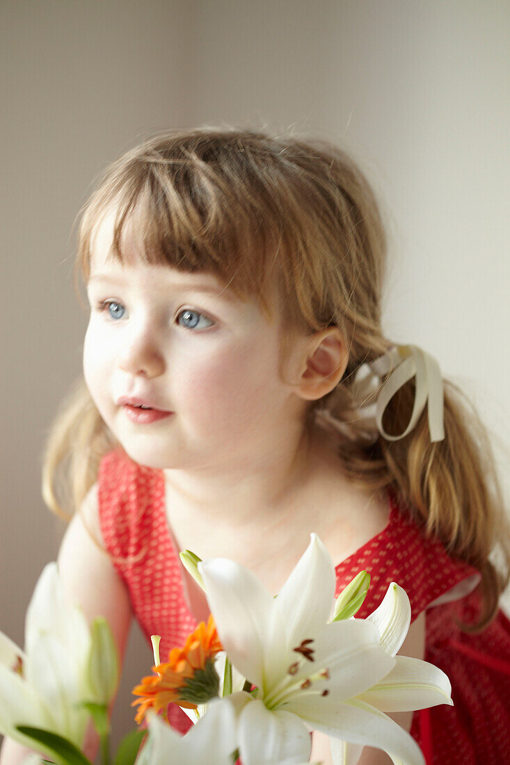 Three year old girl stands in red dress with cut flowers