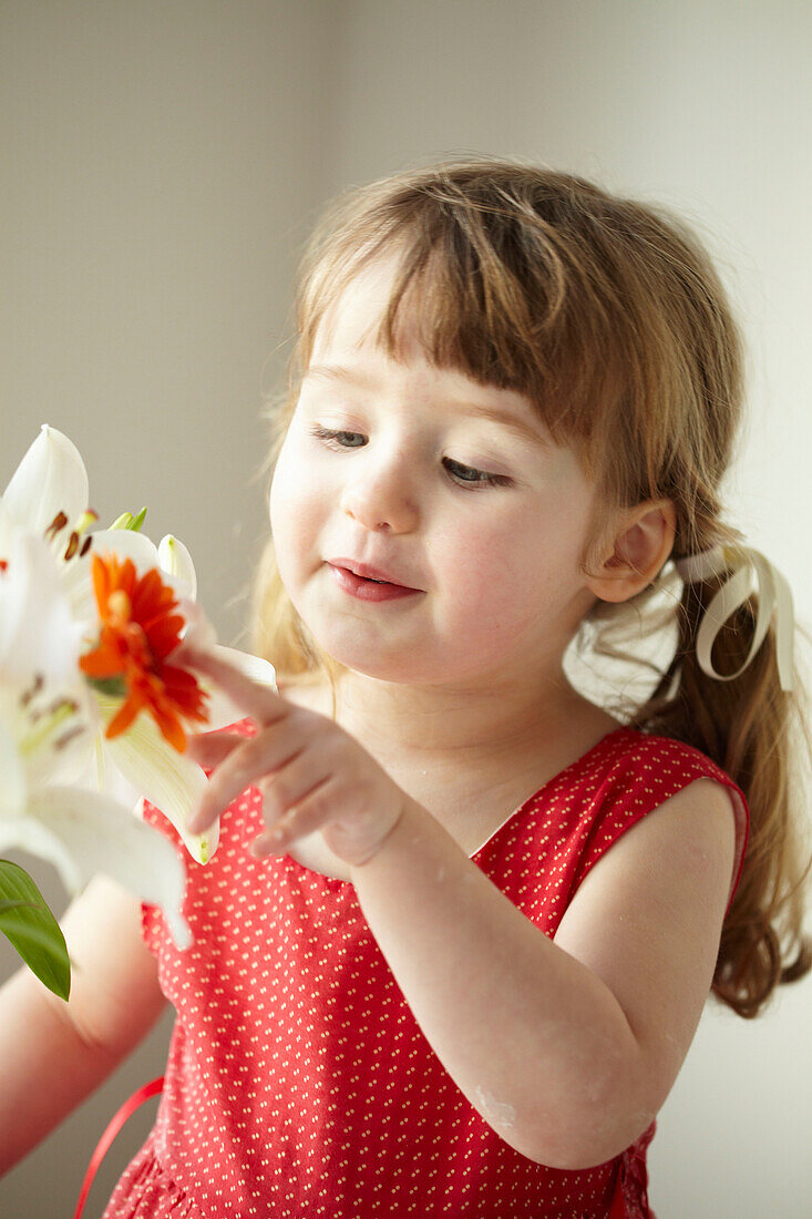 Drei Jahre altes Mädchen steht in rotem Kleid mit Schnittblumen