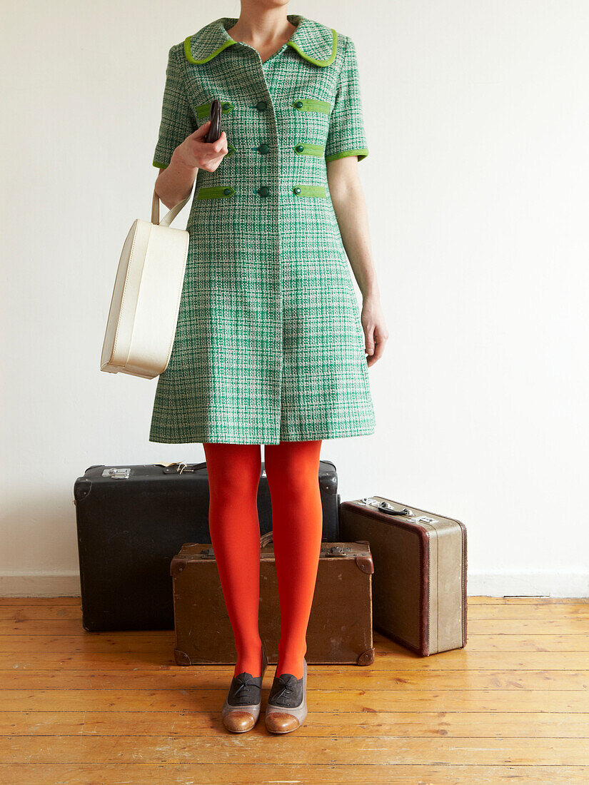Woman in red tights and green dress stands with vintage suitcases