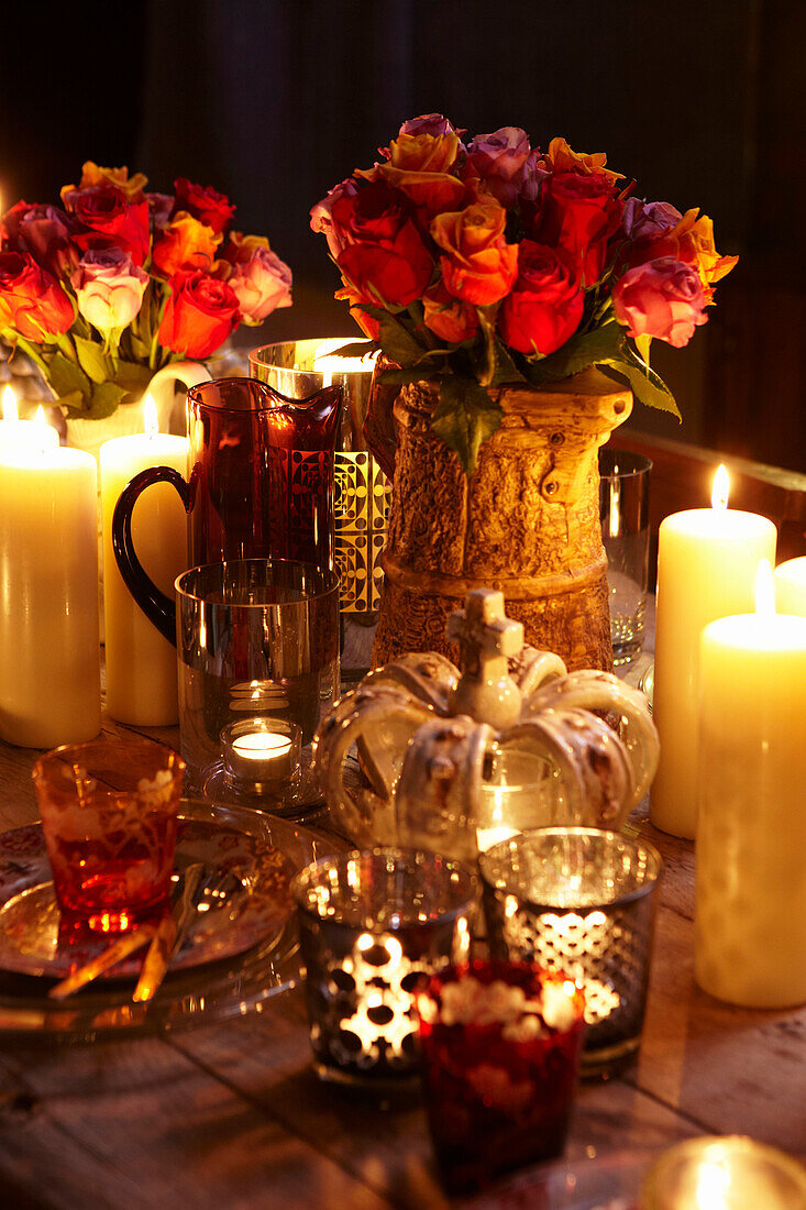 Weihnachtliches Gedeck mit Rosenvasen und Kerzen auf einer Tischplatte