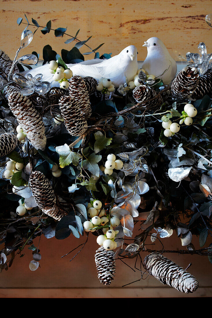 Detail of festive garland draped over the mantlepiece with doves and pine cones amongst foliage