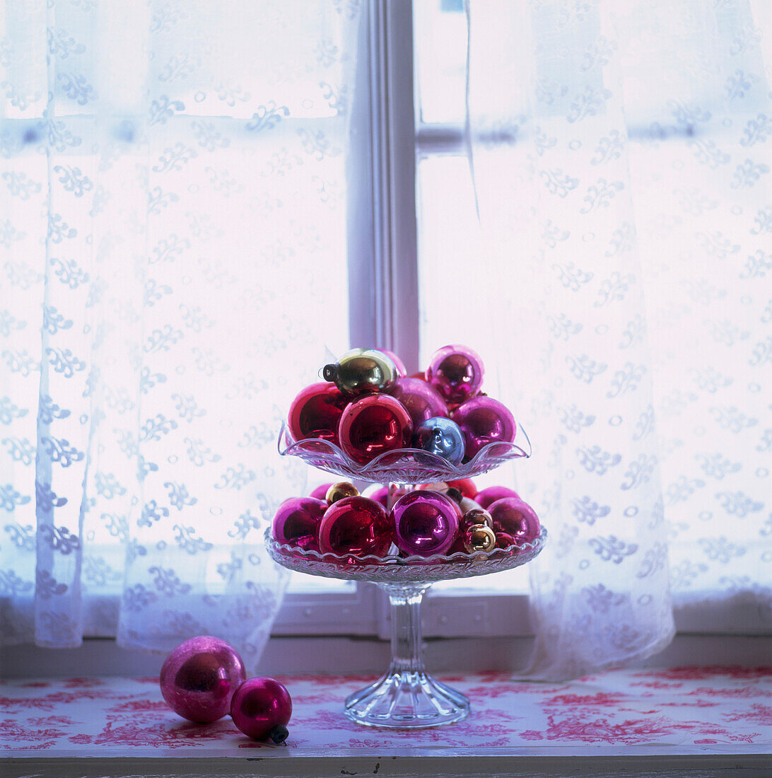 Glaskugeln in einem mehrstöckigen Kuchenständer vor einem Fenster