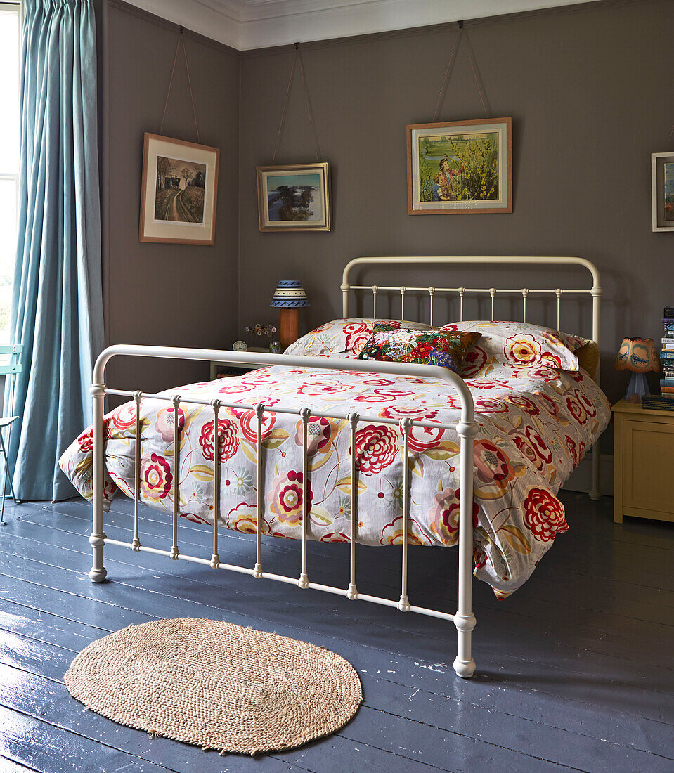 Geblümte Bettdecke auf einem Bett mit Metallrahmen und Kunstwerken in einem Haus der Familie in Rye, East Sussex, England, Vereinigtes Königreich
