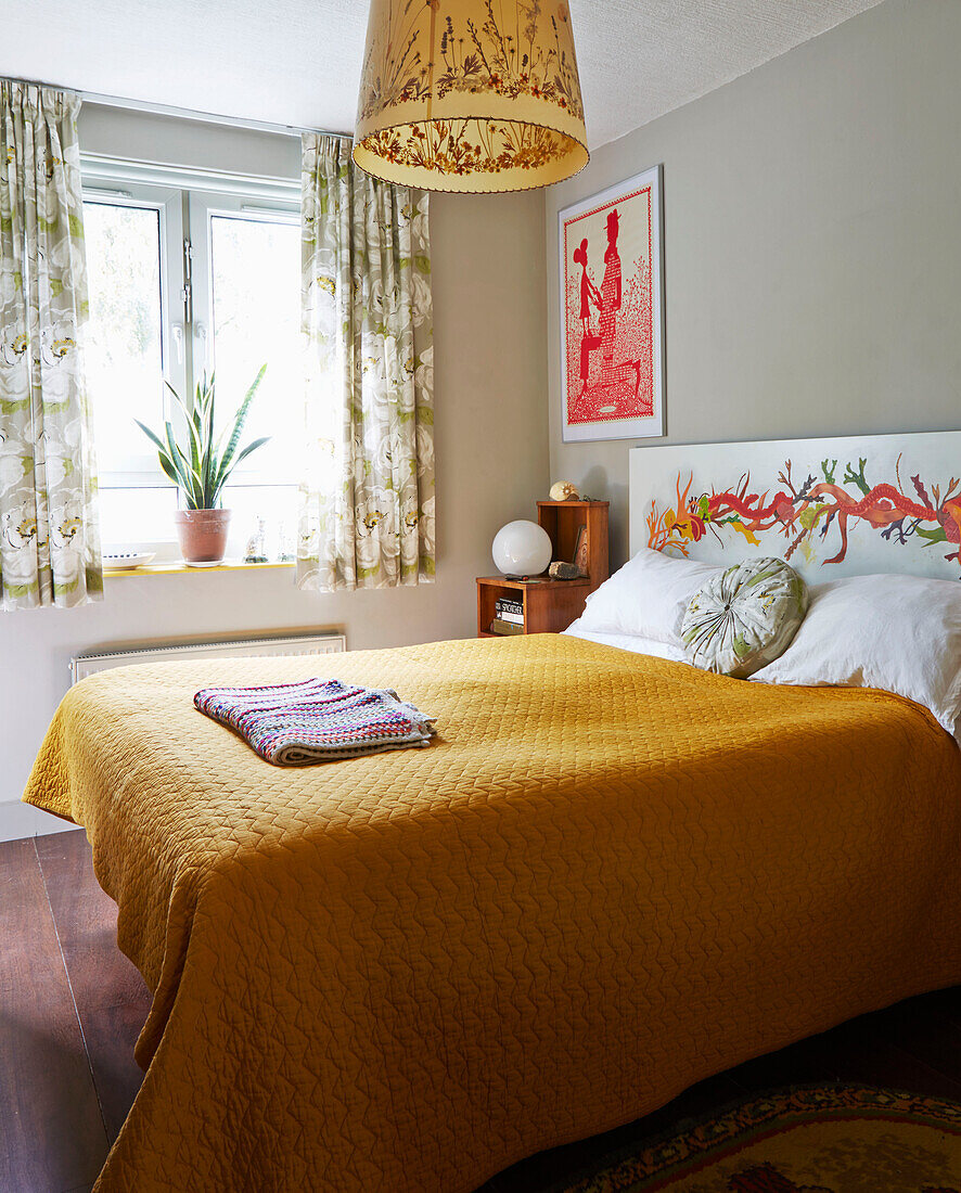 Yellow bedspread with patterned curtains at sunlit window in Hackney bedroom, East London, UK
