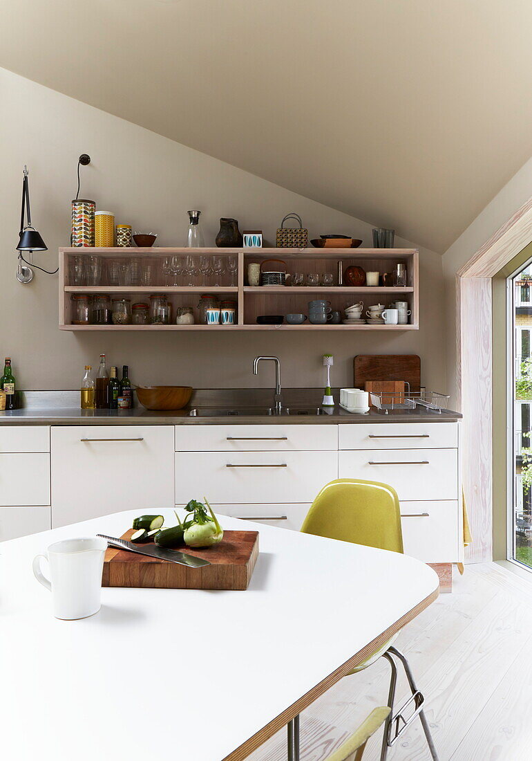 Table and chair with wall mounted shelves in contemporary London kitchen, England, UK