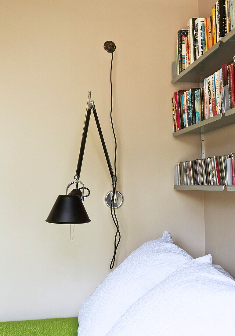 Wall mounted desk lamp with bookshelf in contemporary London bedroom, England, UK