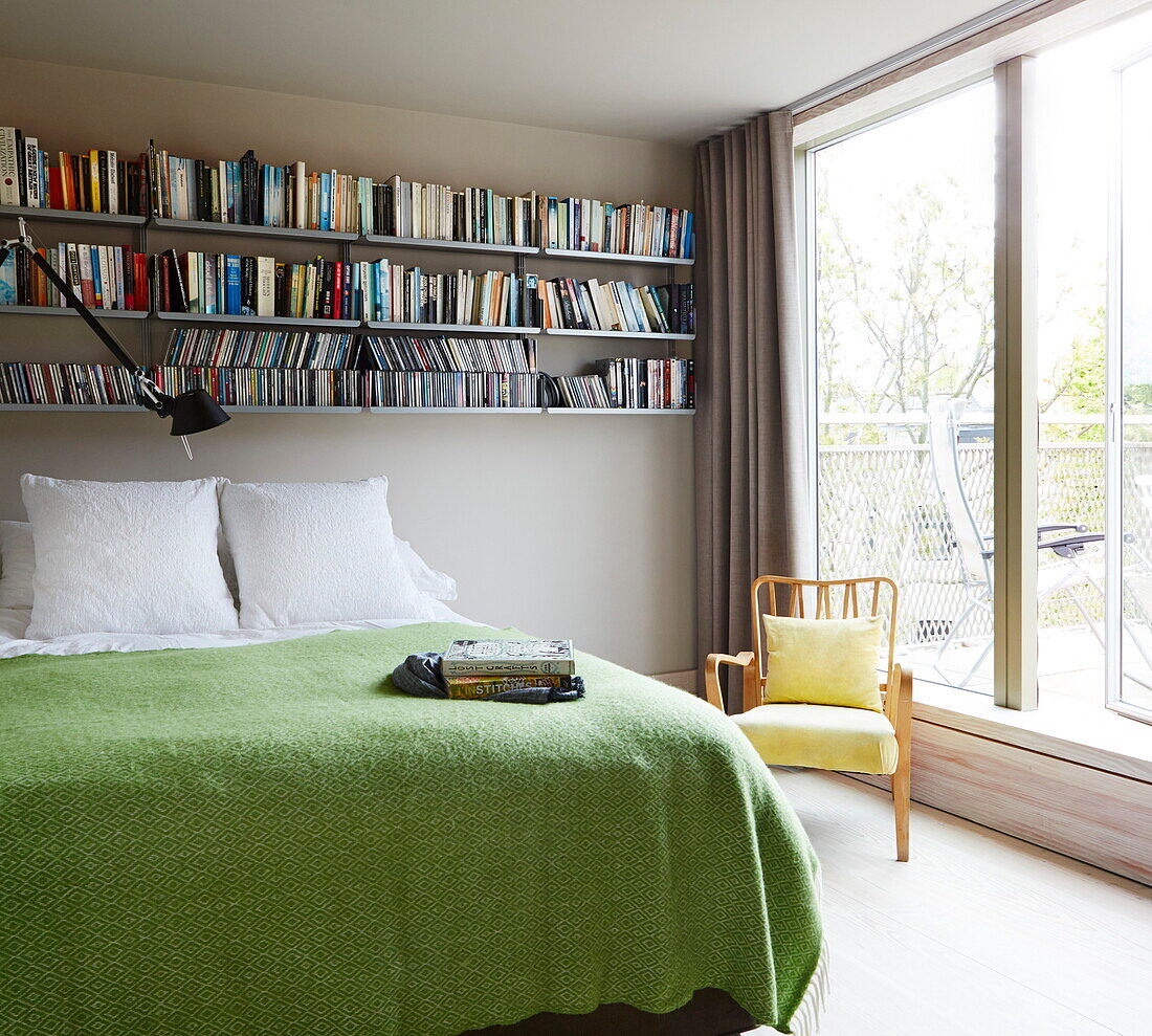 Bookshelves above double bed with green cover in contemporary London home, England, UK