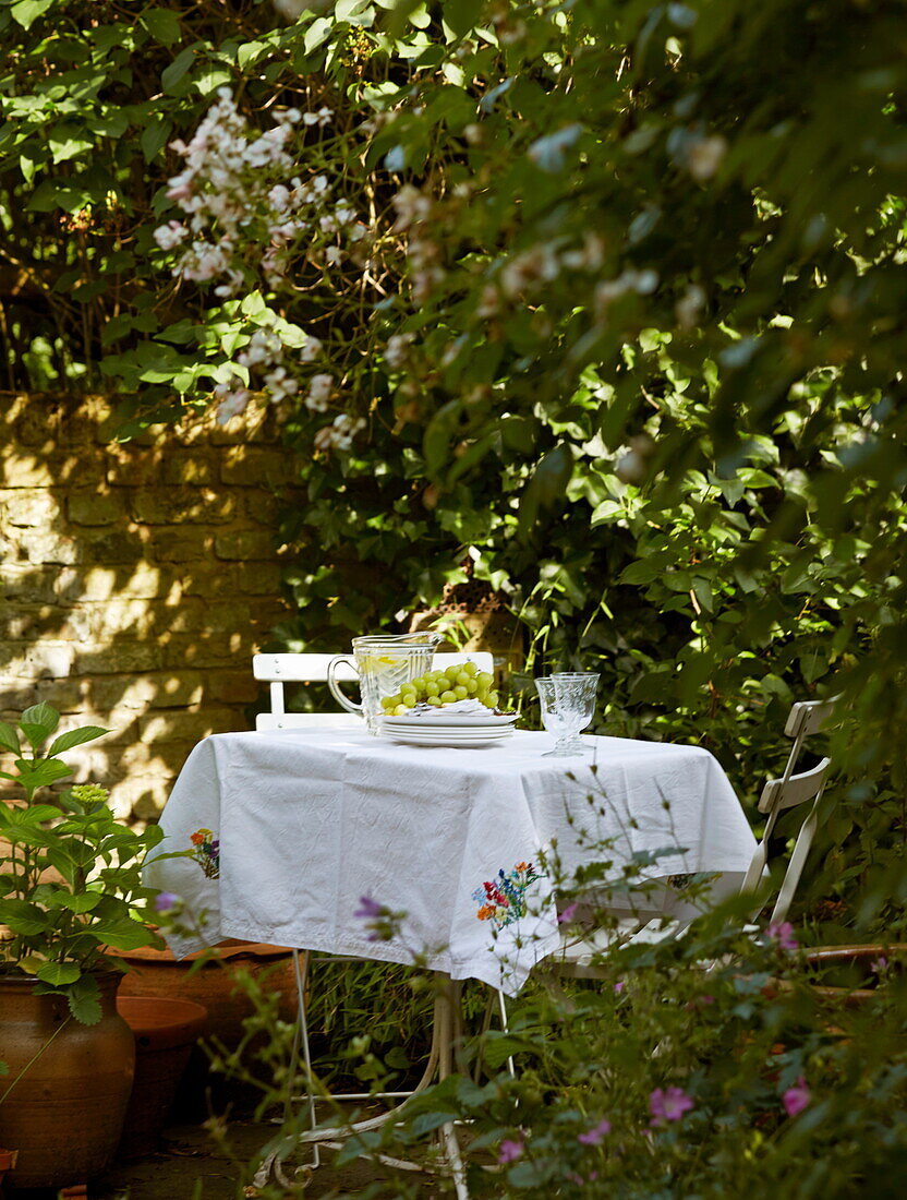 Tisch und Stühle mit weißem Tischtuch und Weintrauben im Garten eines Londoner Stadthauses, England, Vereinigtes Königreich