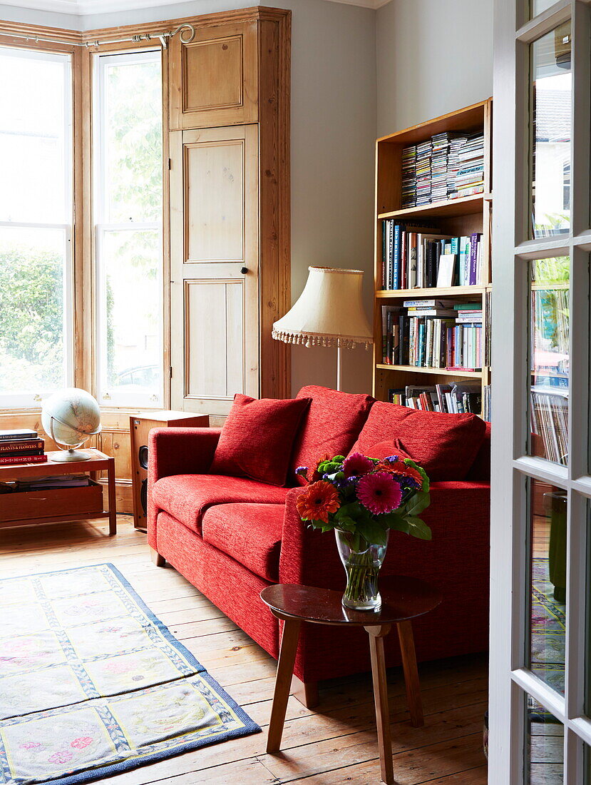 Rotes Sofa und Erkerfenster im Wohnzimmer eines farbenfrohen Hauses in London, England, Vereinigtes Königreich