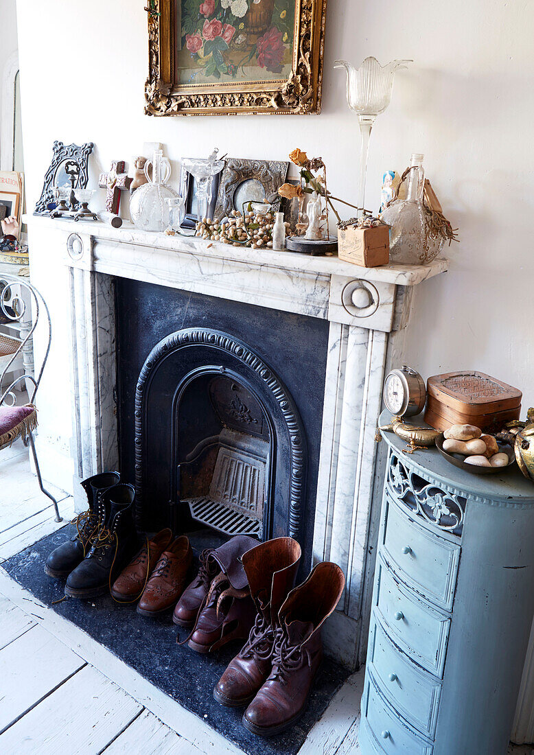 Boots and shoes at fireplace with vintage ornaments in Evershot home, Dorset, Kent, UK
