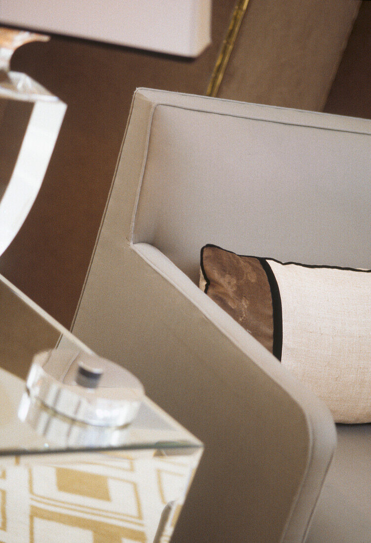 Modernes Polstersofa mit gestreiften Kissen neben einem verspiegelten Glasbeistellschrank mit Tischlampe
