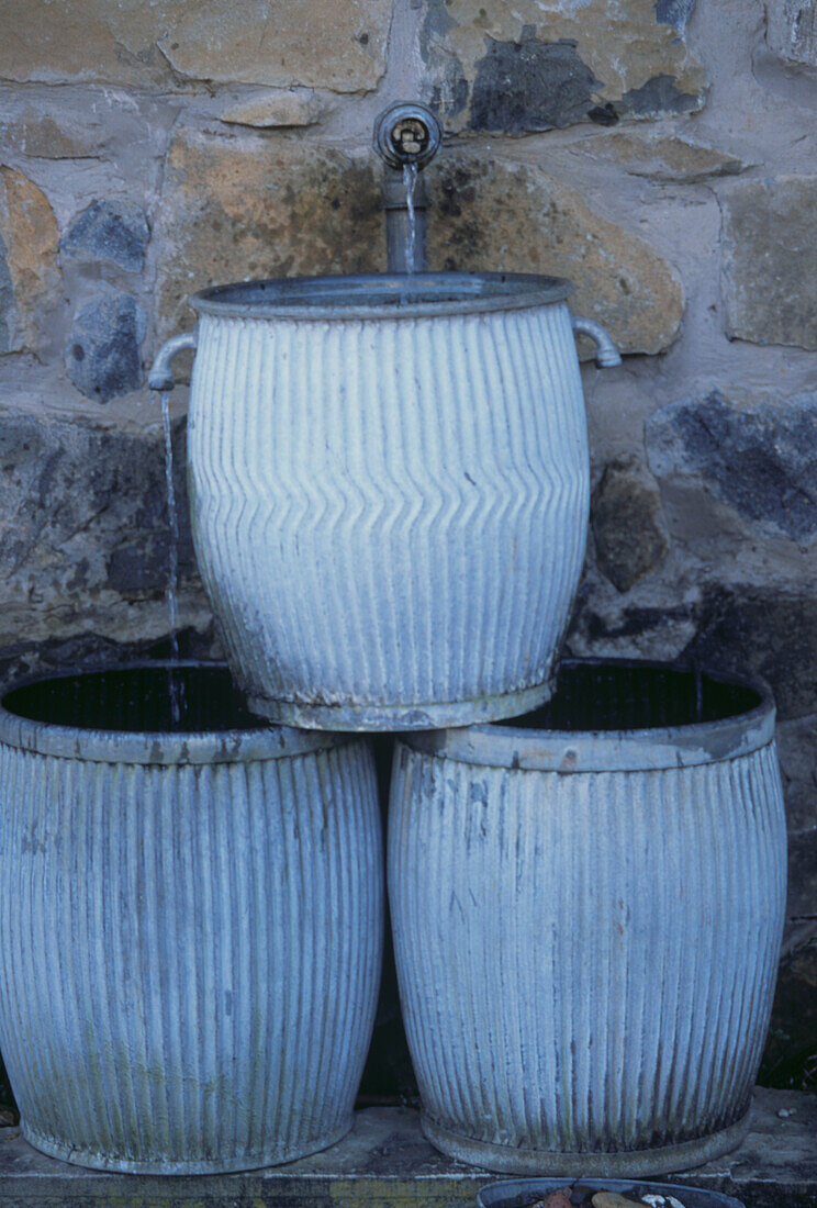 Water feature of decorative lead pots against stone wall