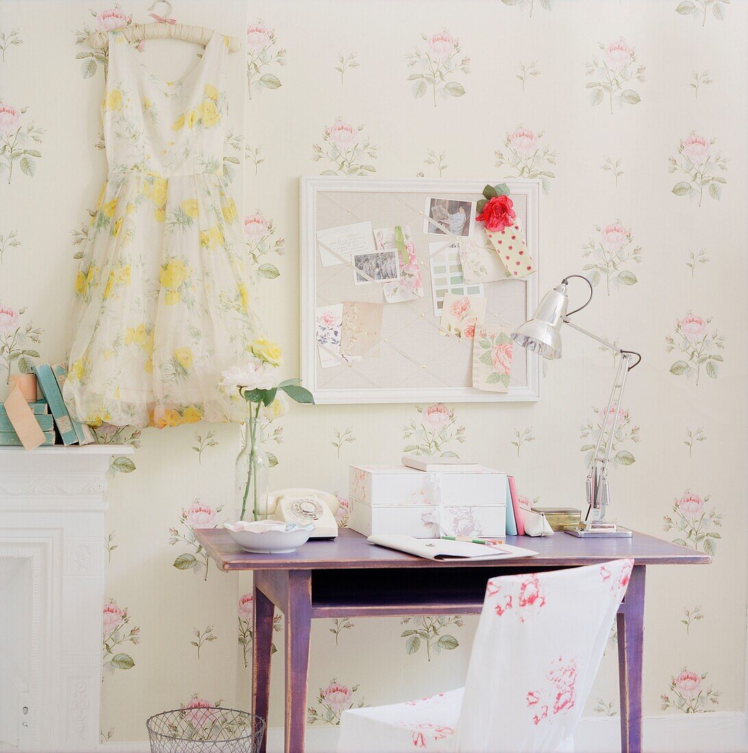 Desk under pinboard with dress in floral wallpapered room