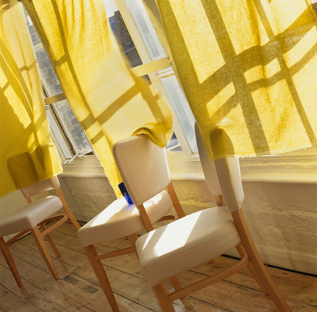 Drei cremefarbene Esszimmerstühle am Fenster mit gelben Vorhängen