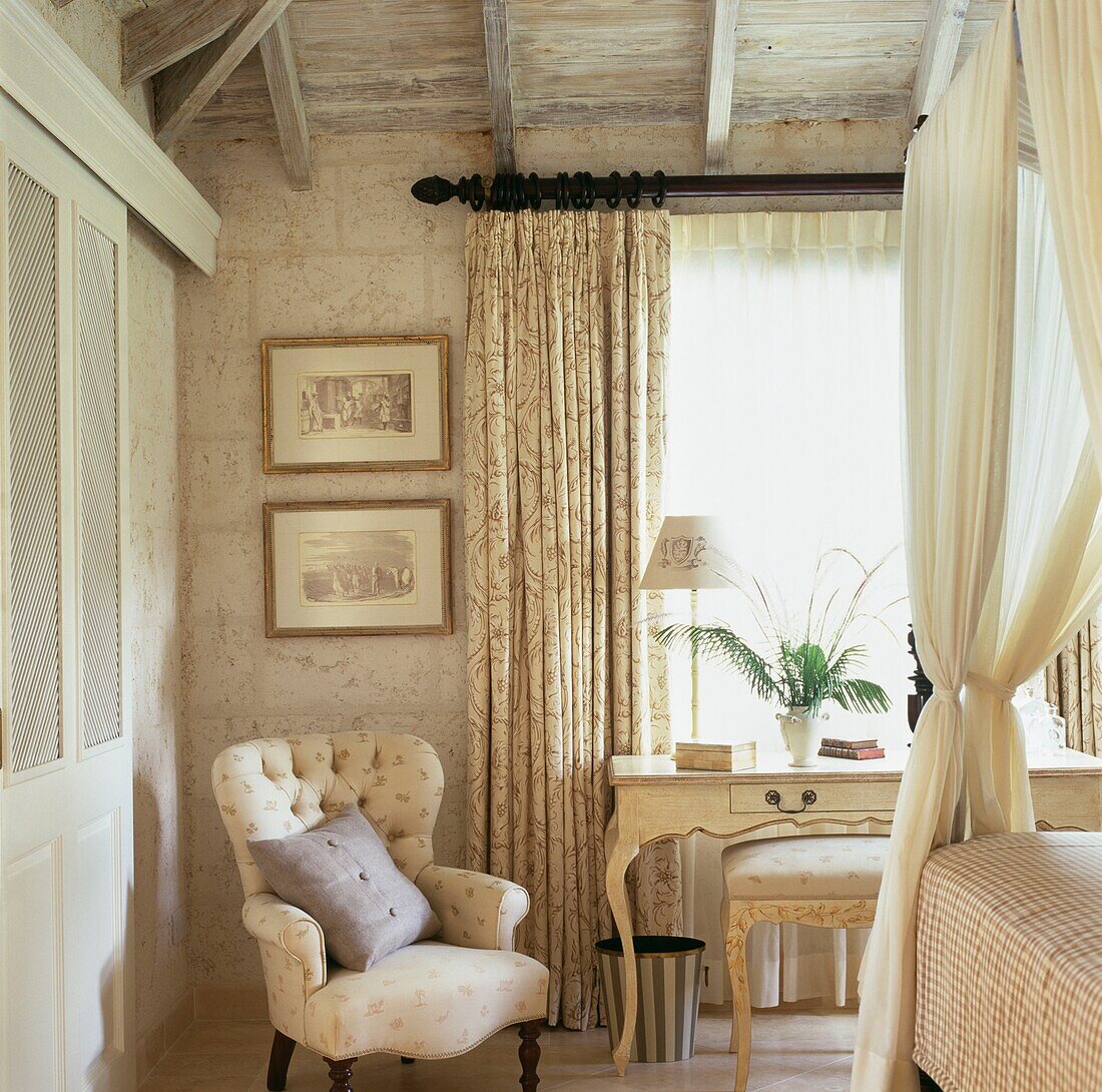 Cremefarbenes Schlafzimmer mit Sessel und Tisch am Fenster und Stoff auf Himmelbett