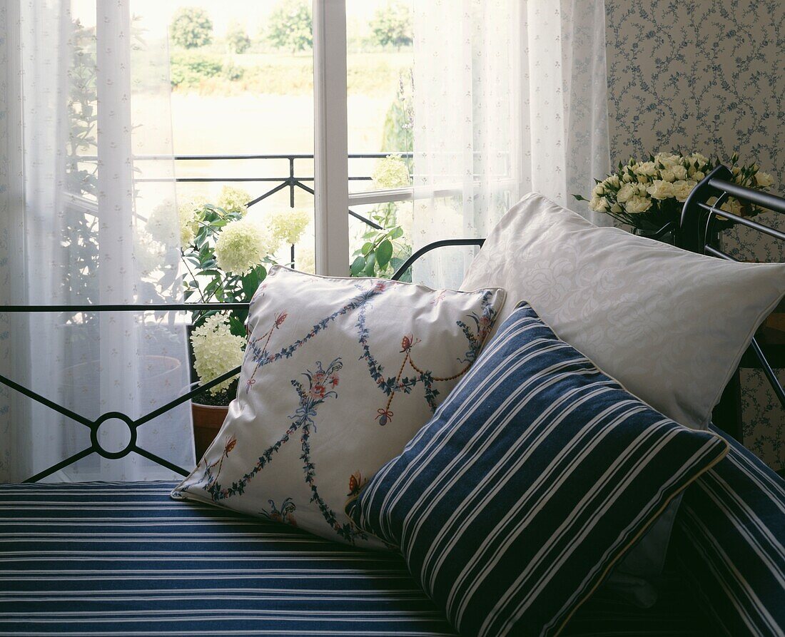 Metall-Tagesbett an der Terrassentür mit farblich abgestimmten Streifen und Kissen
