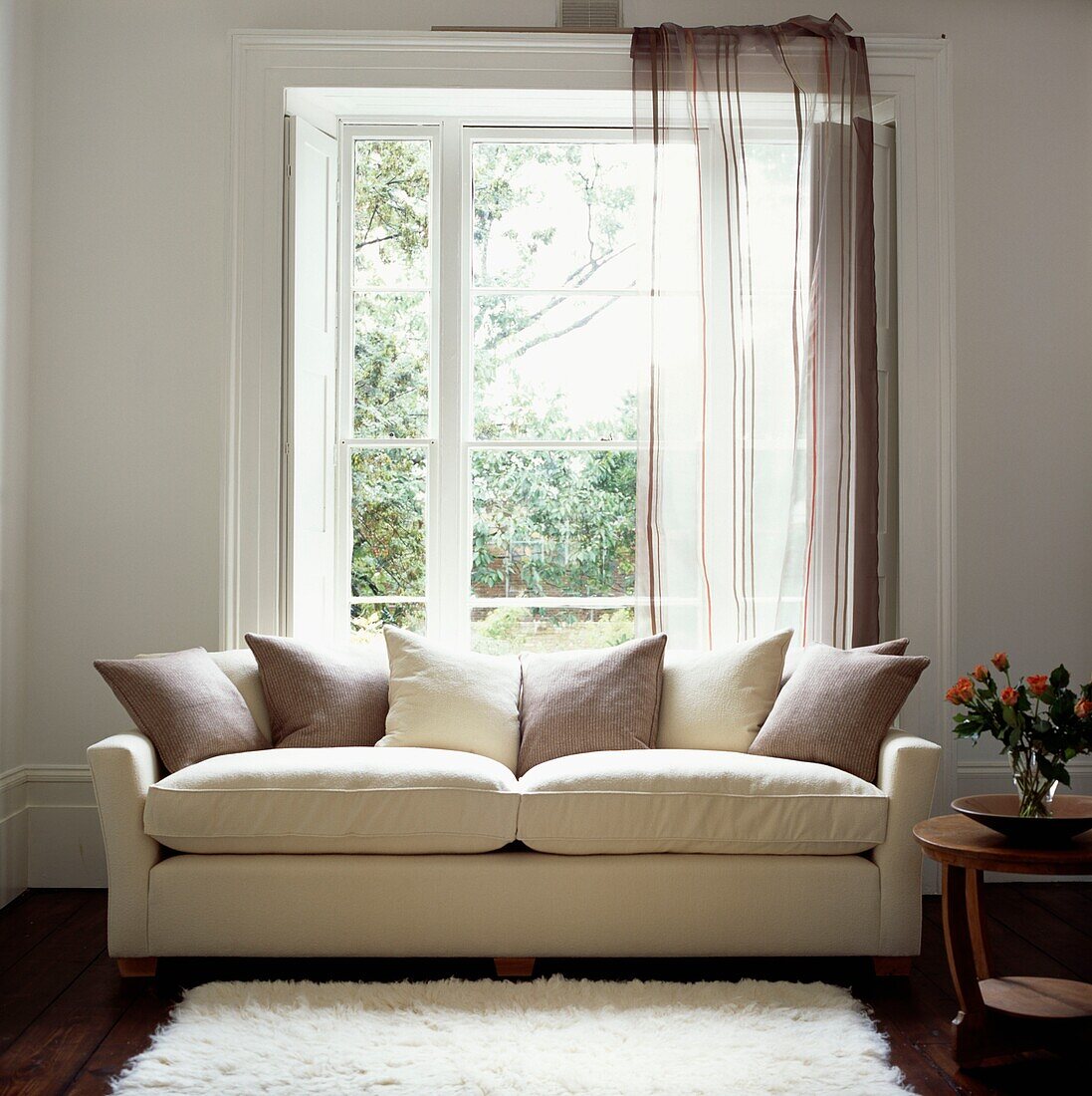 Cremefarbene und hellbraune Kissen auf Sofa am Fenster mit passendem Vorhang