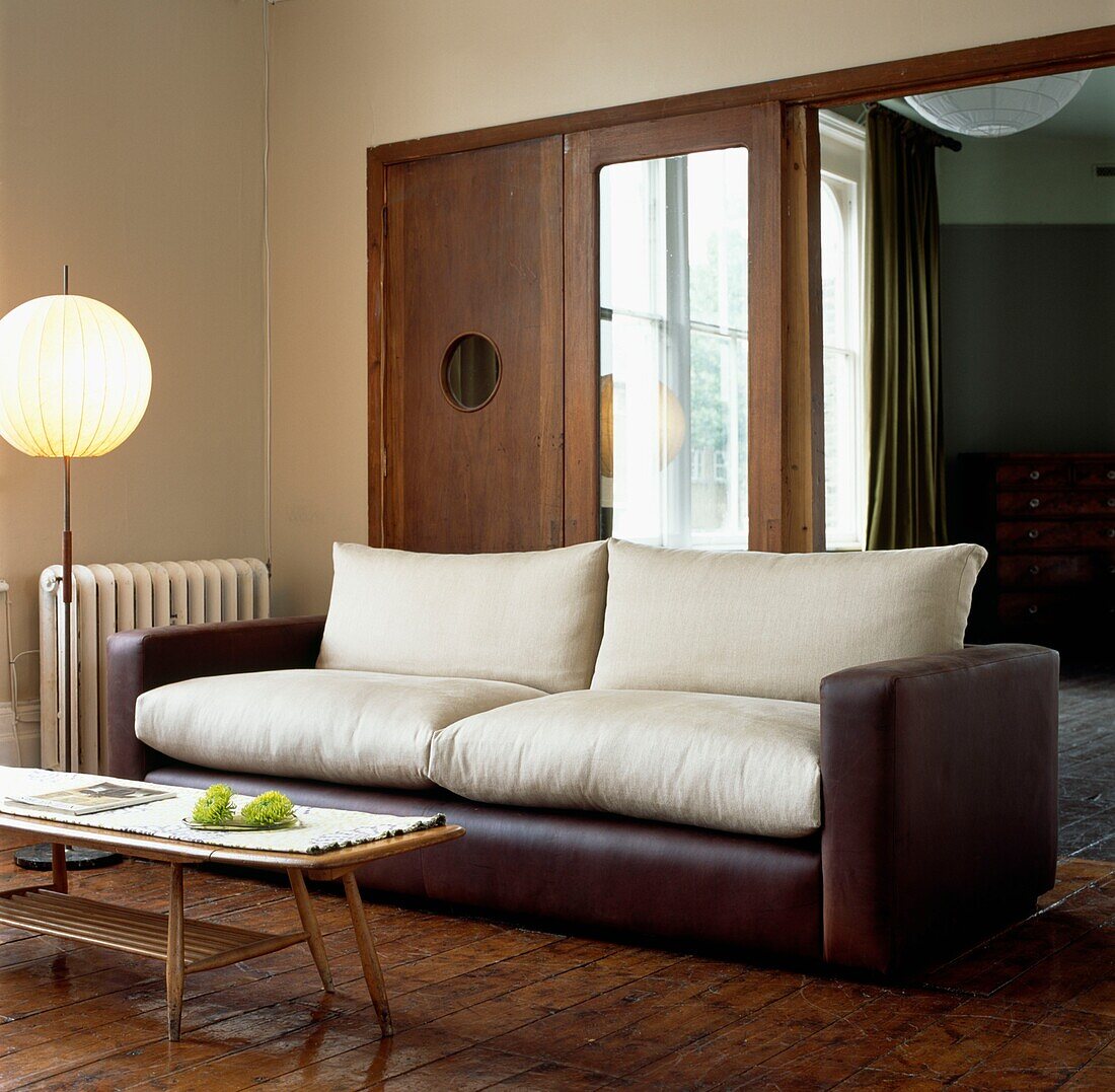 Leather sofa with cream cushions in room with Oriental lamp and wooden doors