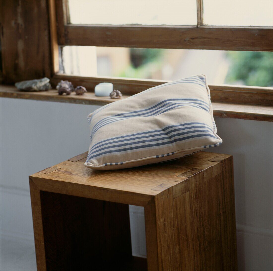 Striped cushion on stool unit at open sash window in unfinished wood