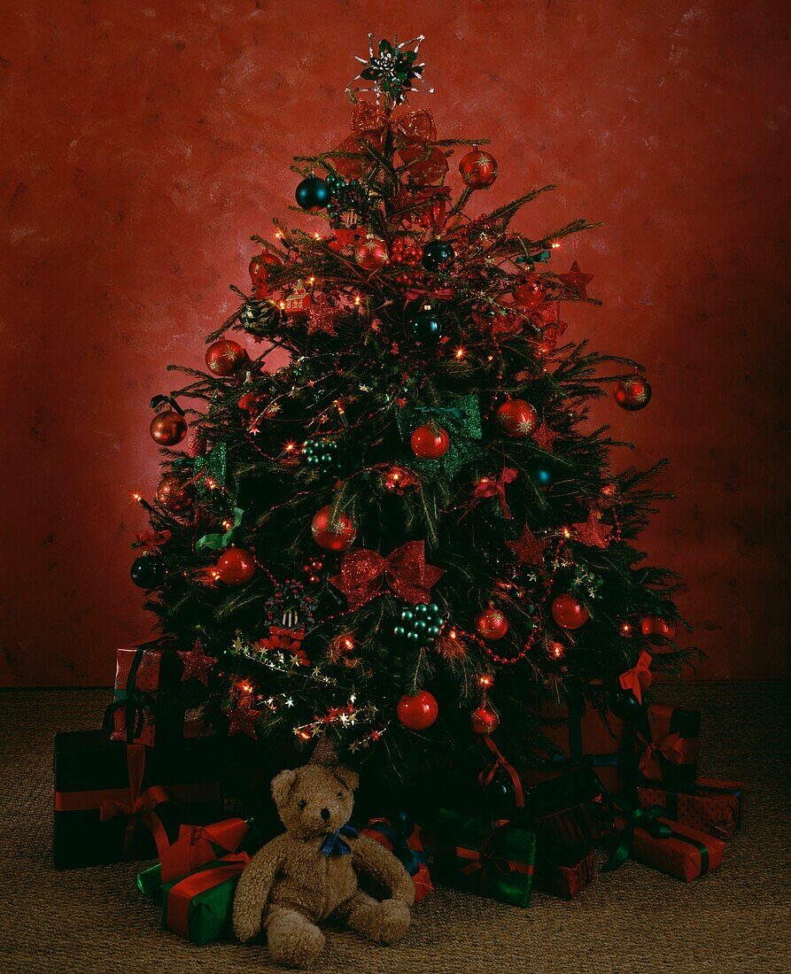 Teddy bear and gifts under Christmas tree decorated with green and red baubles