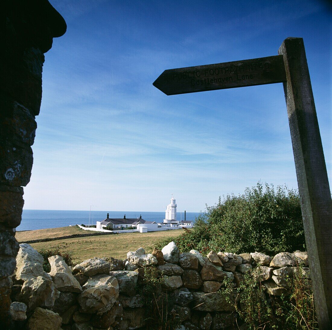 Coastal lighthouse viewed from a stone wall with road sign
