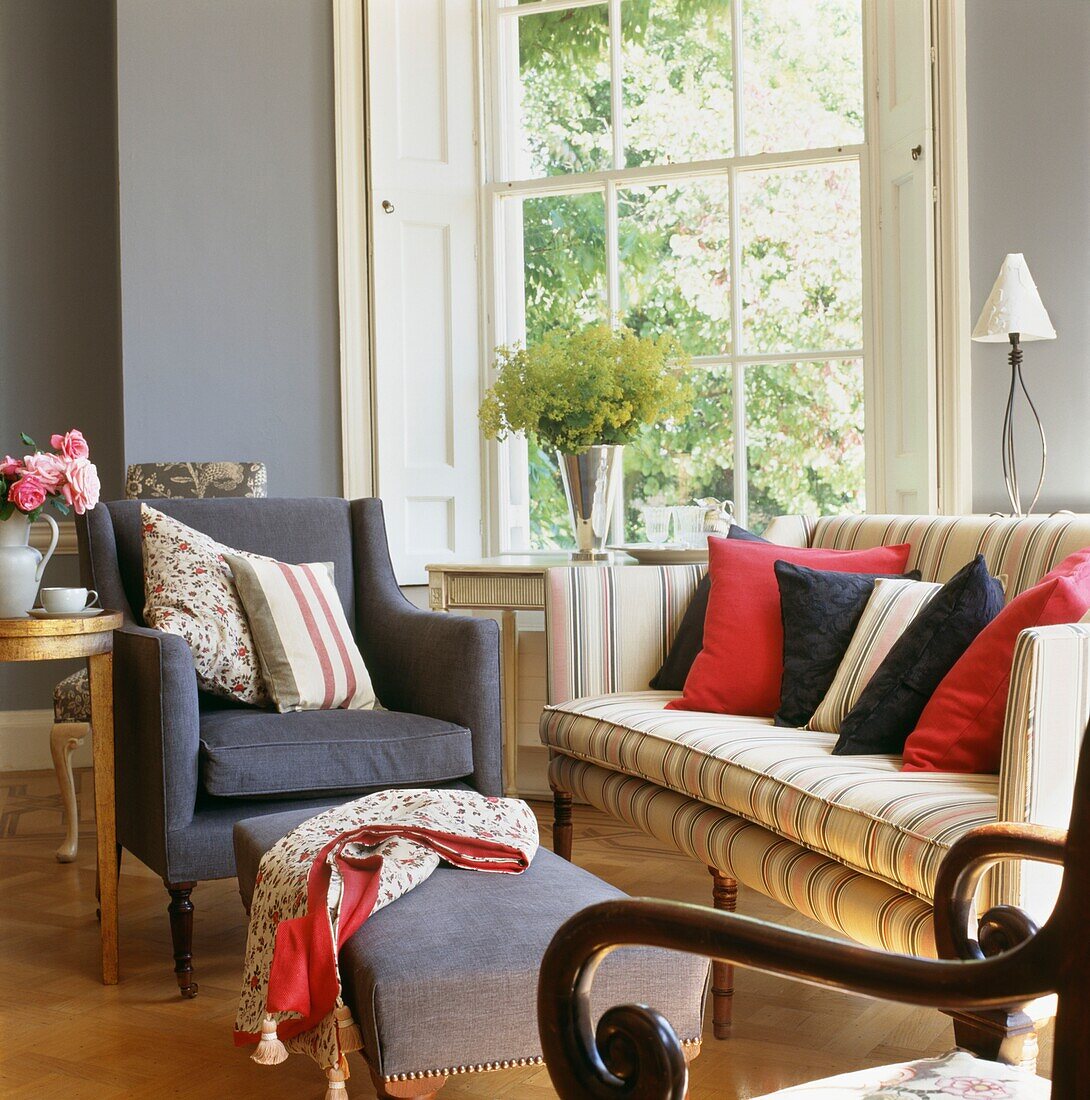 Contrasting cushions on striped sofa at window with grey upholstered armchair
