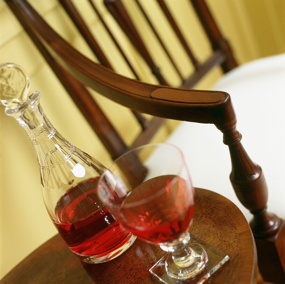 Weinglas und Dekanter mit Rose auf einem Holzhocker neben einem Stuhl