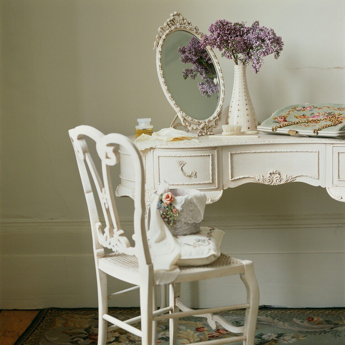 Vase of flowers with oval shaped mirror on dressing table with chair and handbag