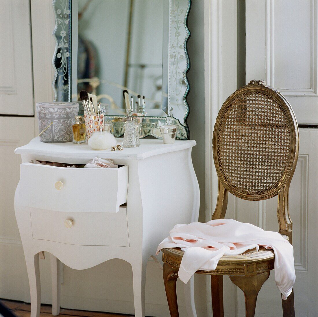 Rosa Bluse auf antikem Stuhl neben Schminktisch mit graviertem Spiegel und offener Schublade