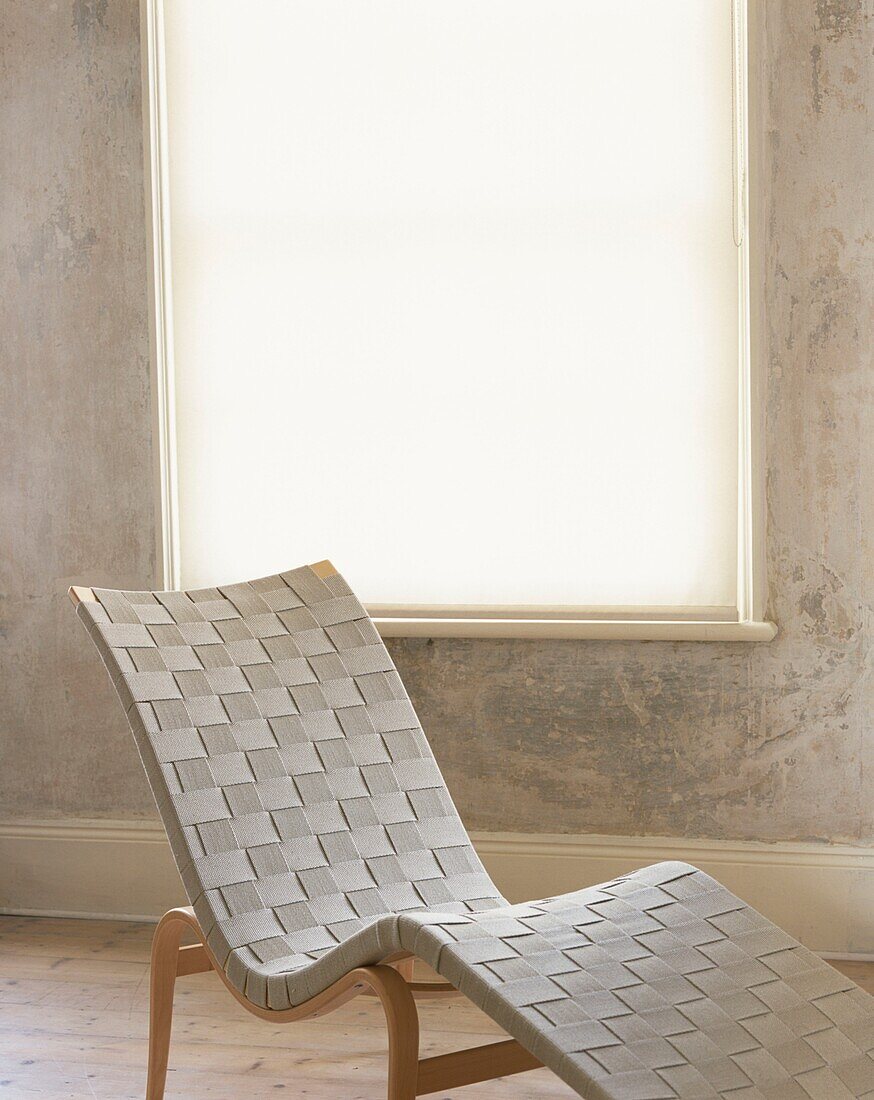 Weißer Sessel und geschlossene Jalousien in einem Raum mit unvollendeten Gipswänden