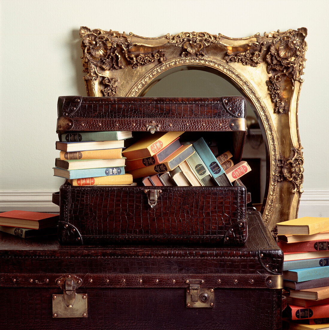 Koffer aus Krokodilleder mit alten Büchern und einem vergoldeten Spiegel im Rokoko-Stil im Hintergrund