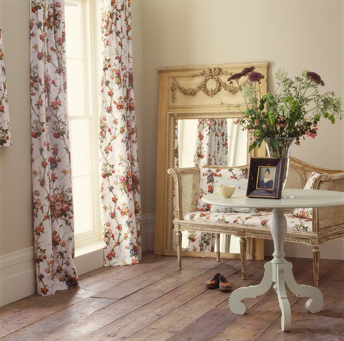 Hübsche geblümte Vorhänge und großer Spiegel mit Schilfrohrliege und rundem Beistelltisch mit frischen Blumen
