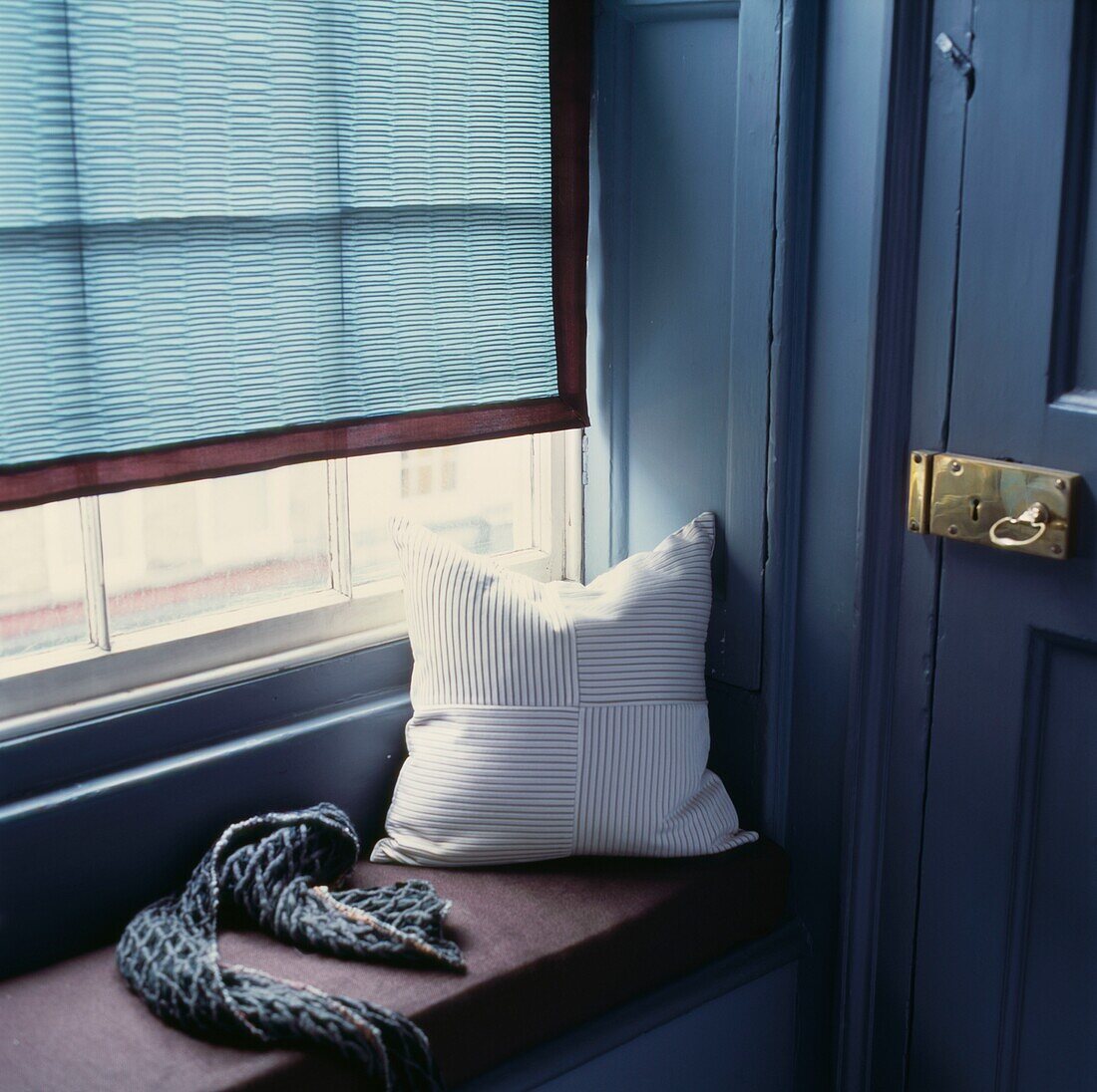 Kissen und Schal auf der Fensterbank mit türkisfarbener Jalousie und Messingschloss und Schlüssel