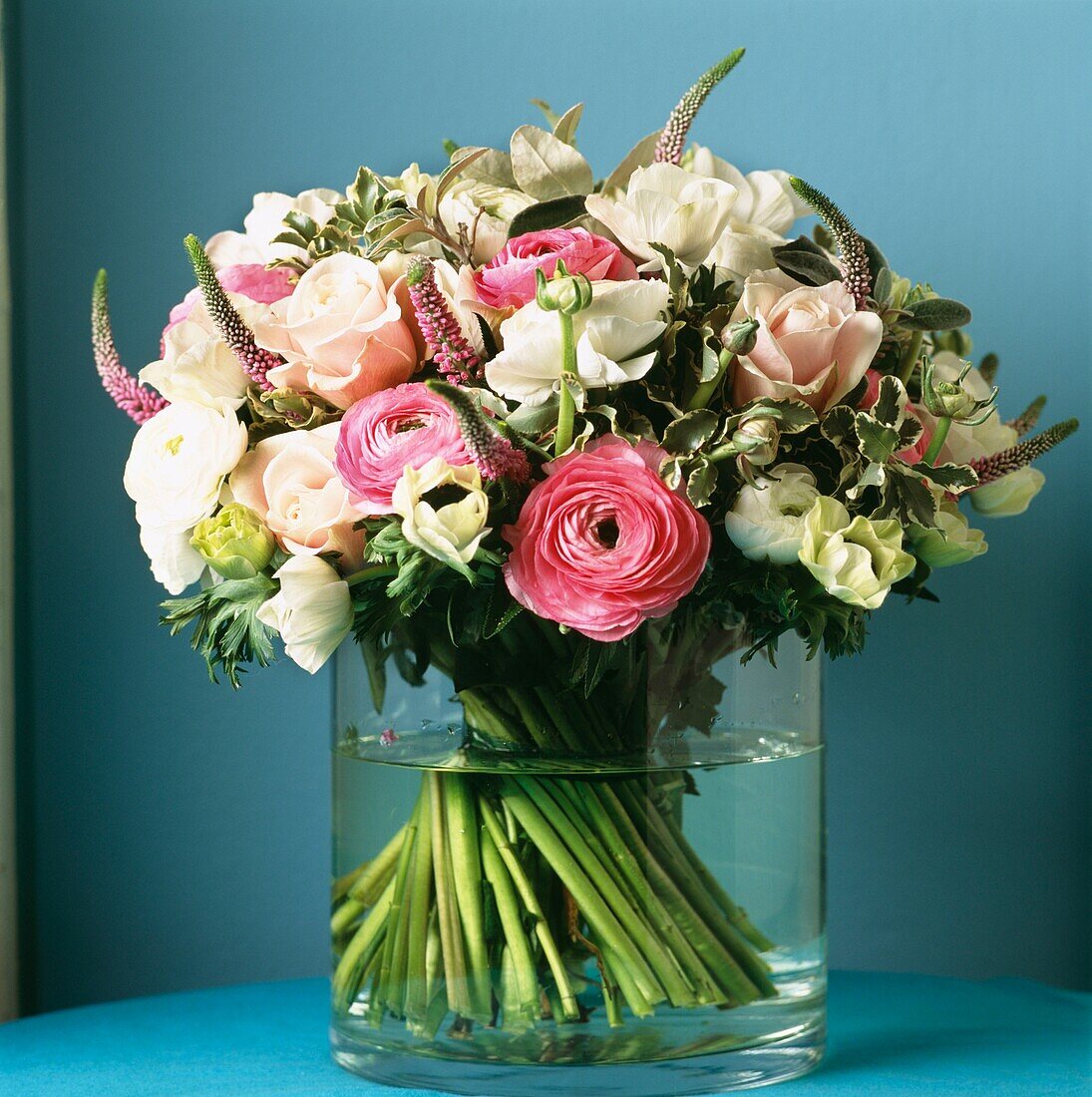 Blumenstrauß aus rosa und weißen Blumen in Glasvase vor türkisfarbener Wand mit Wiesenehrenpreis, Ranunkeln, Kronenanemonen, Klebsame und Rosen