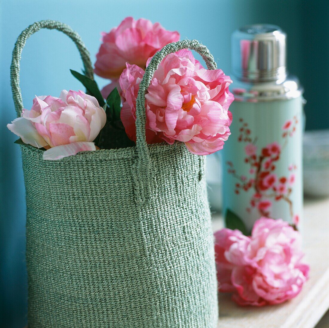 Rosa Blumen in pastellgrüner Einkaufstasche mit floral gemustertem Flachmann