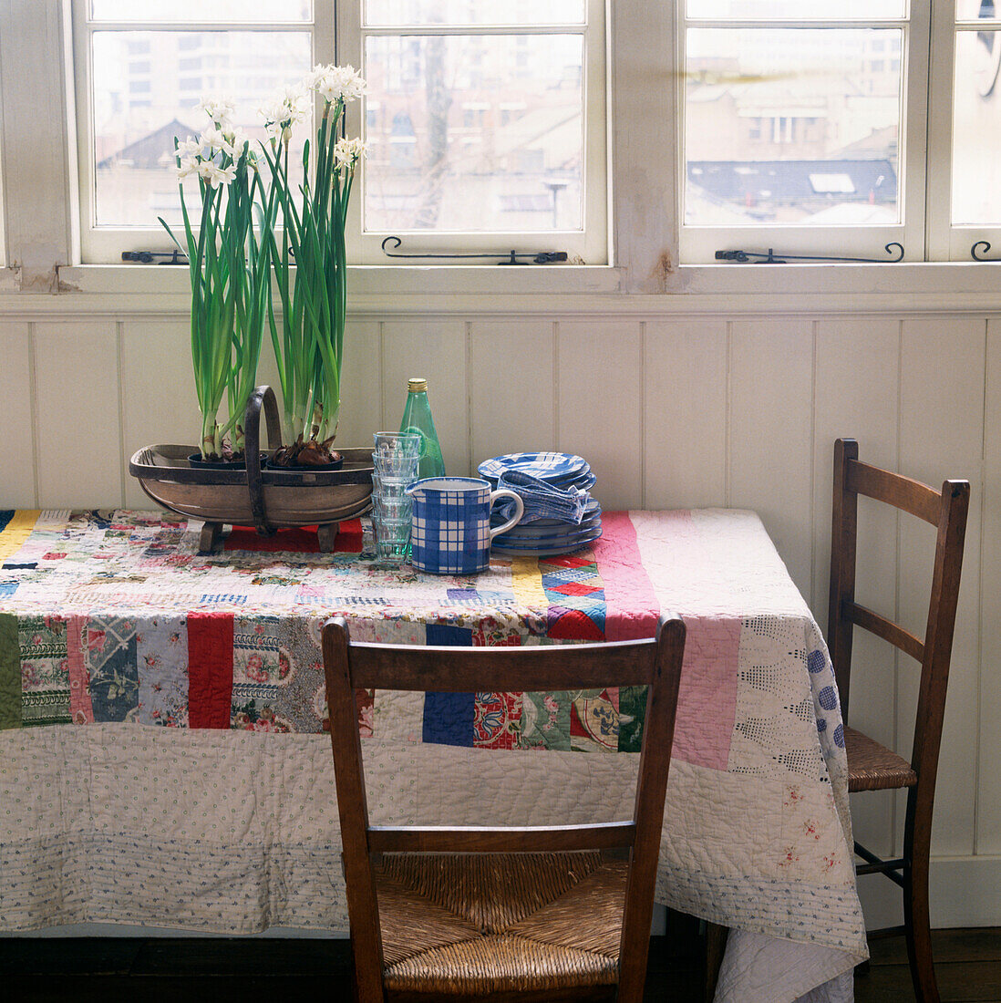 Küchentisch in einem getäfelten Raum mit Narzissen auf einer farbenfrohen Patchwork-Tischdecke