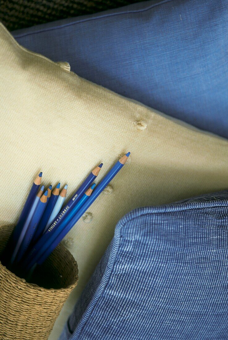 Blaue Buntstifte in einem geflochtenen Behälter vor blauen und weißen Polstern