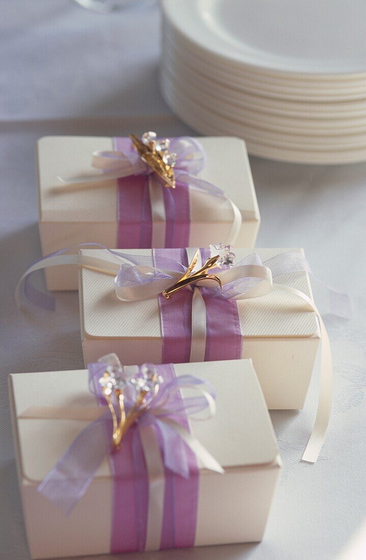 Weiße, mit lilafarbenen und weißen Bändern gebundene und mit Swarovski-Kristallglasblumen verzierte Geschenkboxen