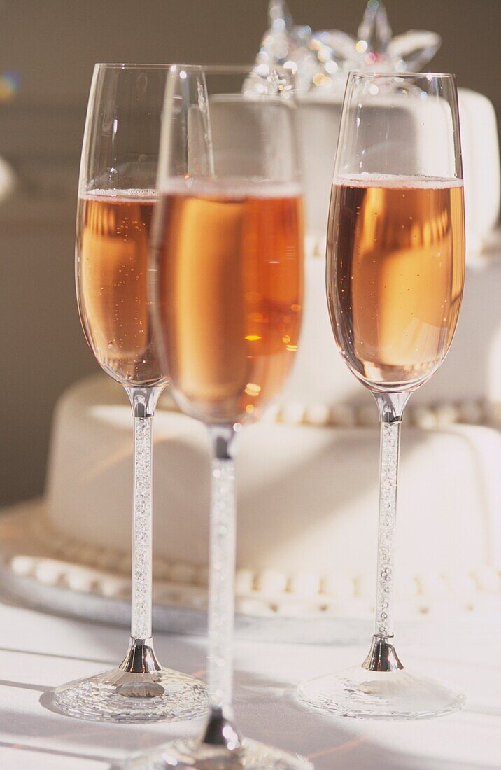 Close up of pink champagne and tiered wedding cake