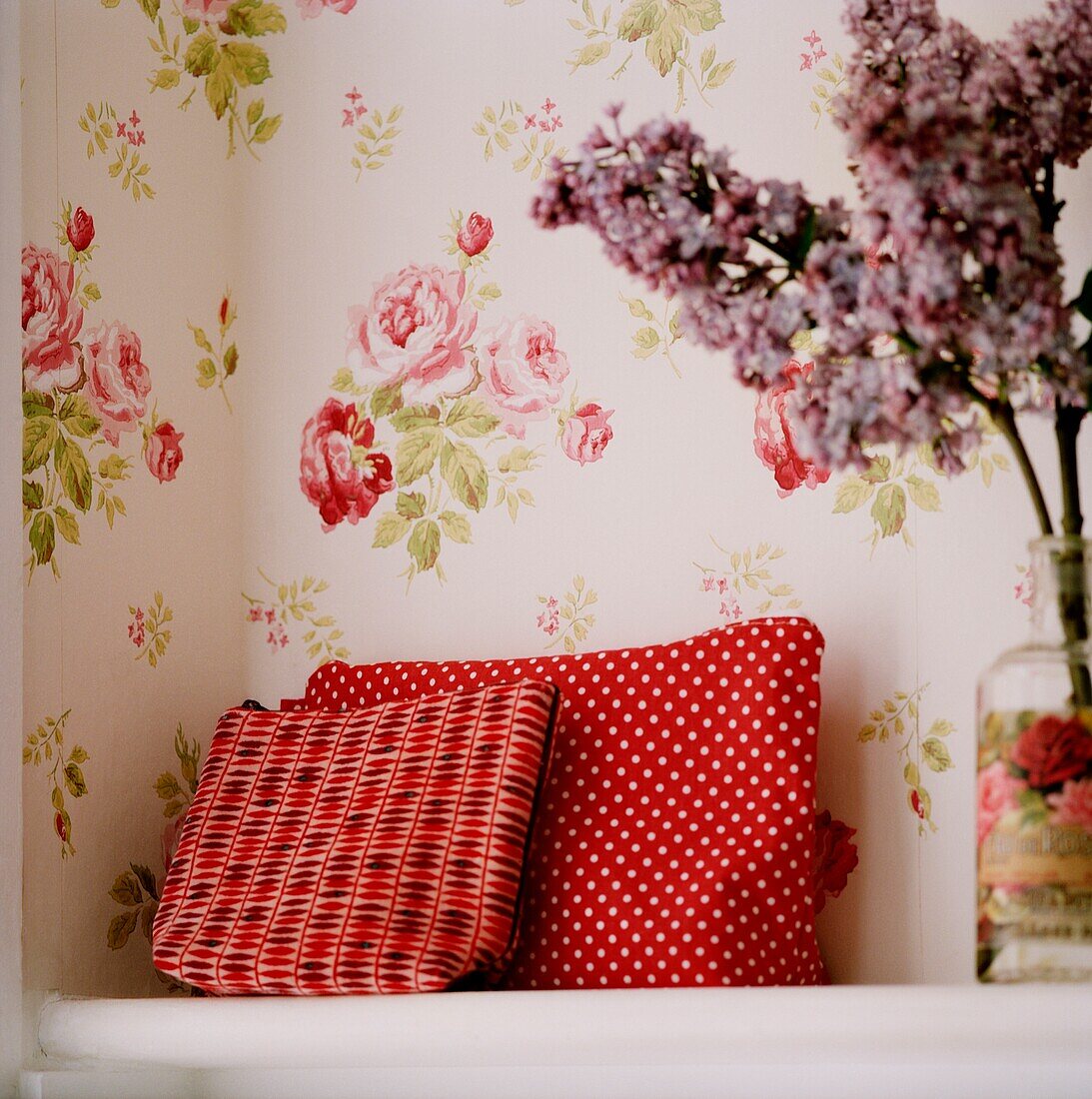 Red washbags with lilac on shelf with floral wallpaper