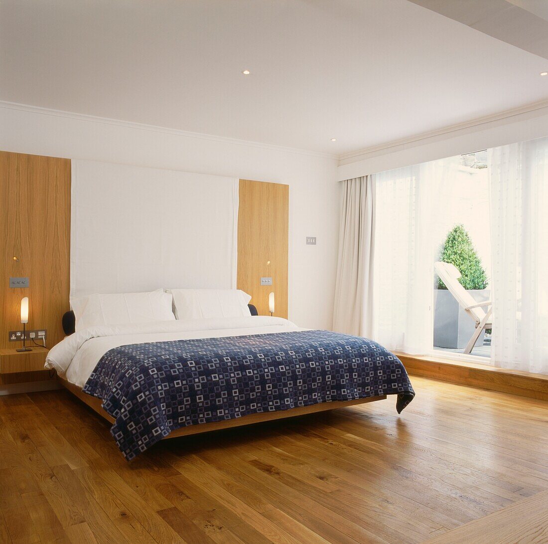 Doppelbett mit Schränken und Fußboden aus hellem Holz und offener Schiebetür zur Außenterrasse