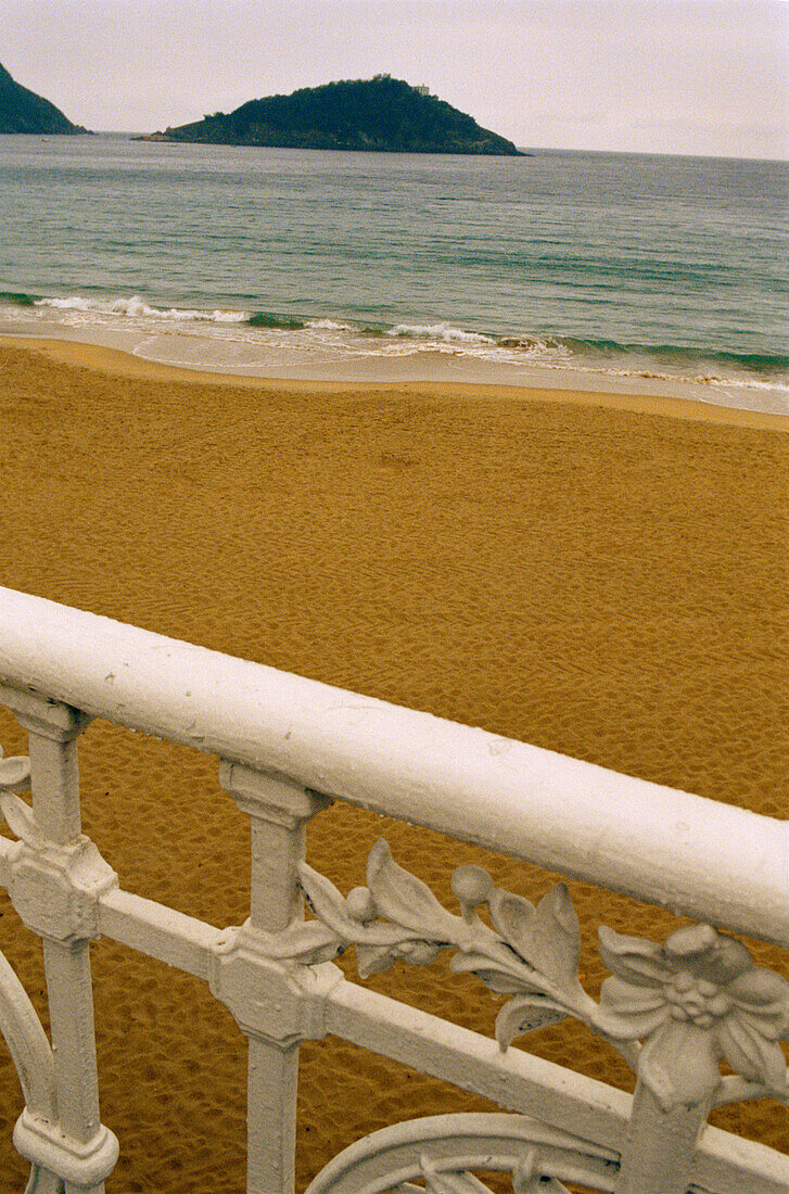 Dekoratives Eisengeländer am berühmten Strand von La Concha in San Sebastian mit der Insel Isla de Santa Clara in der Ferne