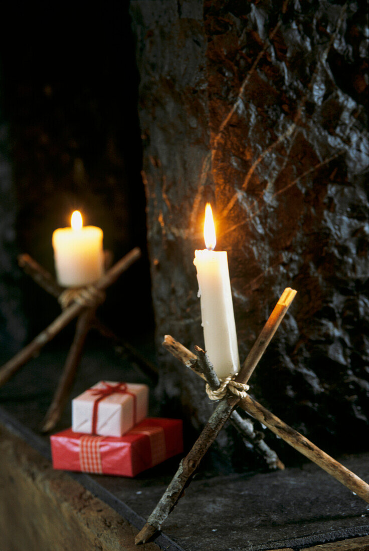 Kerzen in Zweighaltern neben einem Steinkamin mit Geschenken