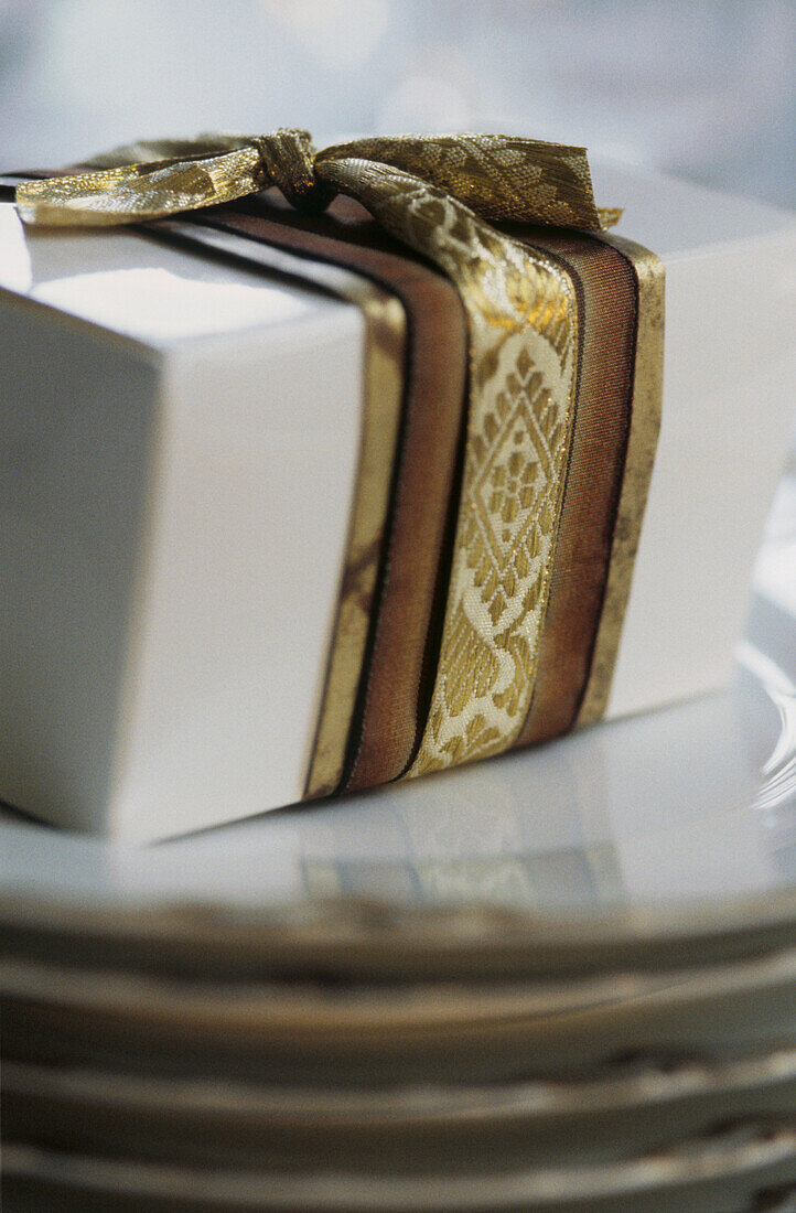 Close up of Christmas present with patterned gold ribbon on white wrapping paper 
