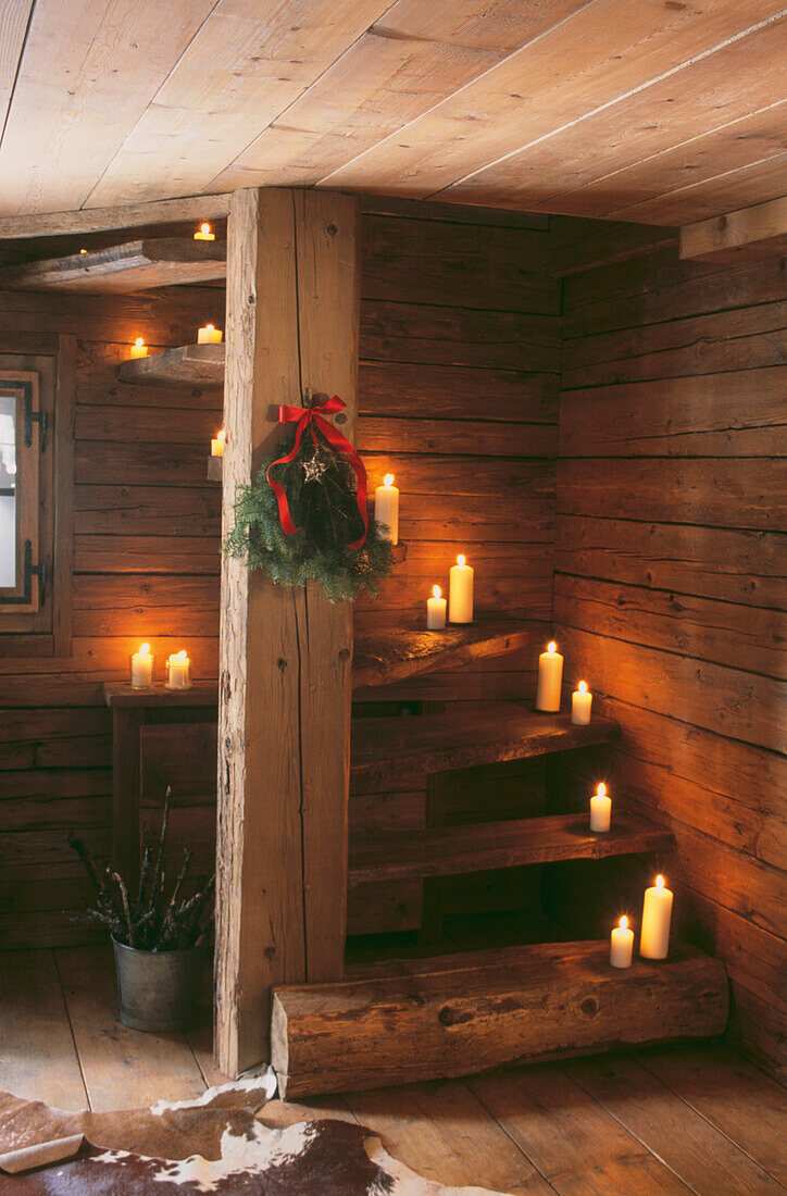 Beleuchtete Kerzen und Weihnachtsfichtenzweig auf Holztreppe in Holzchalet