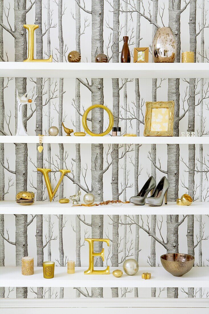 Still life with tree silhouette wallpaper and gilt letters on a white shelf with group of metallic objects