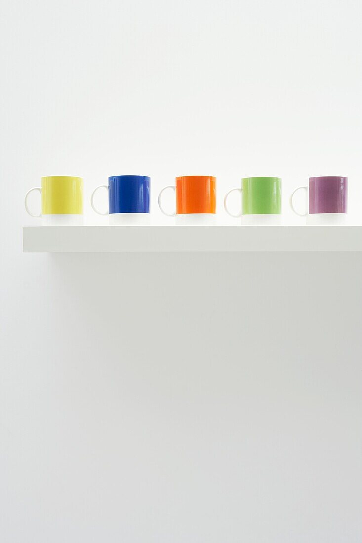 Five brightly coloured cups on a white shelf