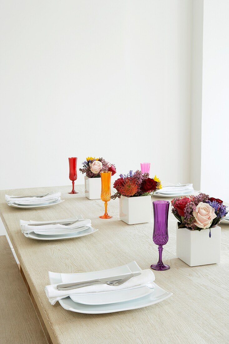 Gedeckter Tisch in einem weißen Raum mit bunten Gläsern und Blumendekoration