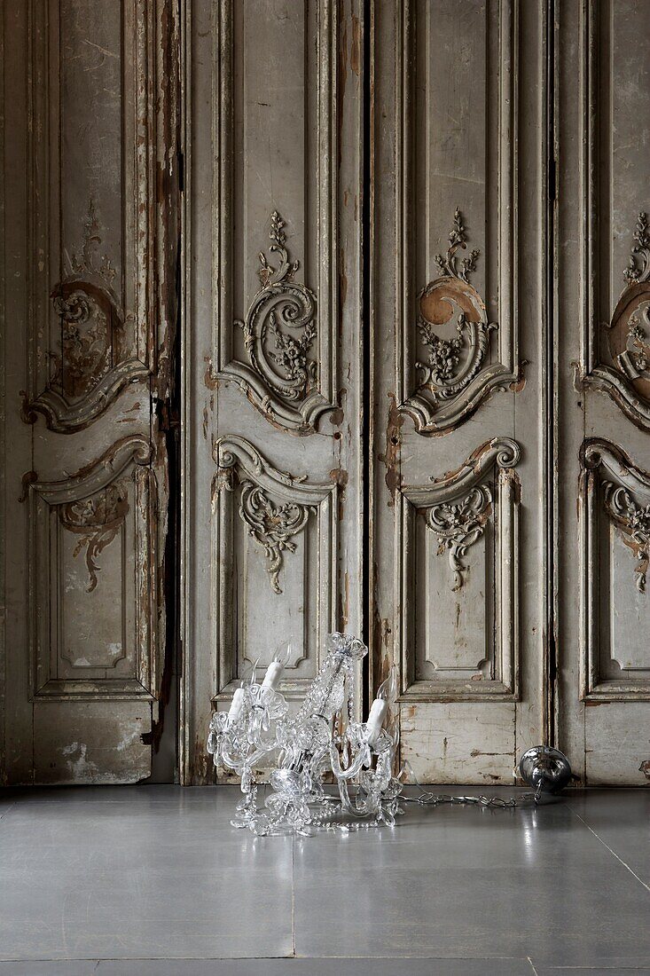 Glaskronleuchter auf dem Boden mit verschnörkelter, holzgetäfelter Wand im Rokokostil